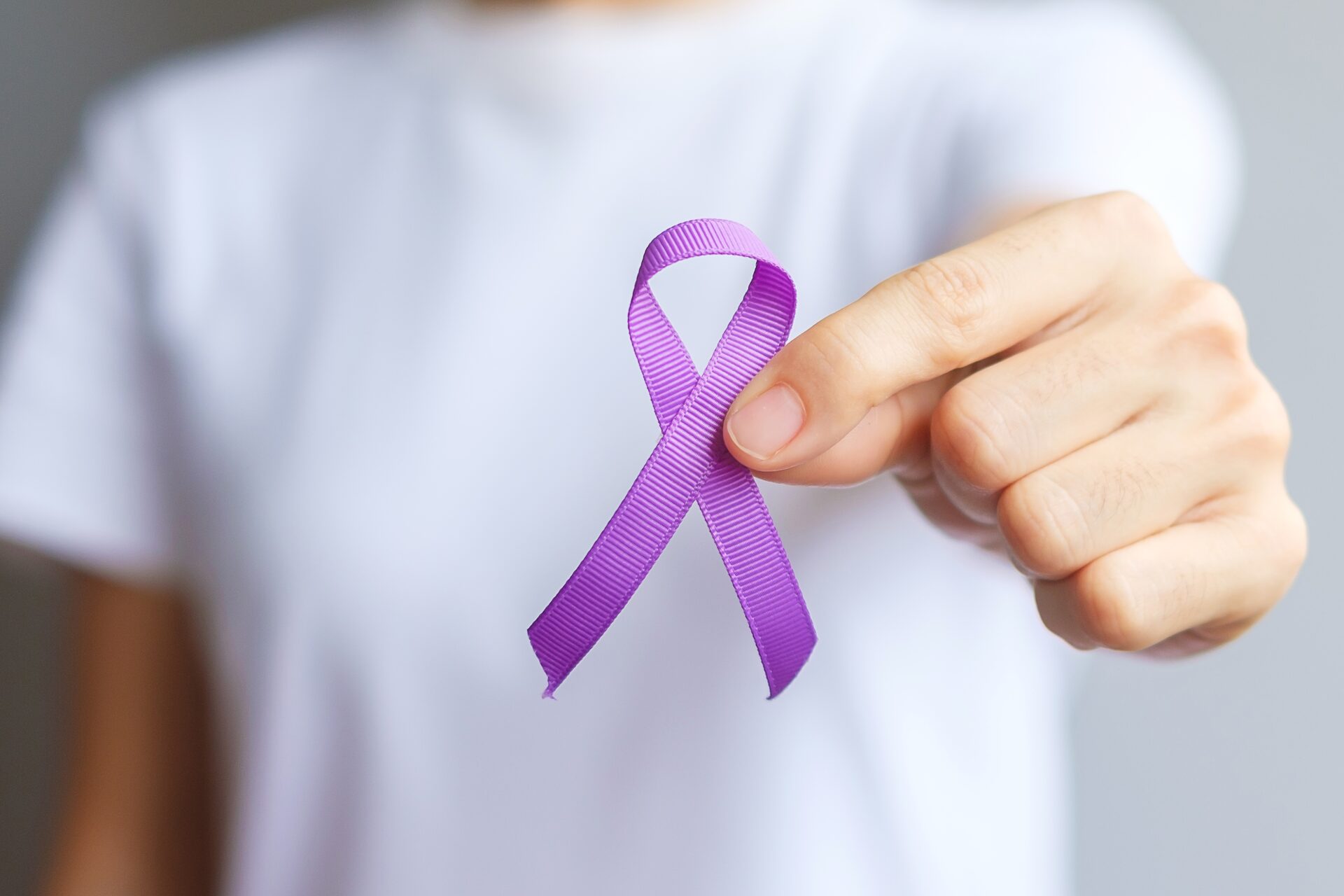 Hand holding purple Ribbon for Pancreatic, Esophageal, Testicular cancer, world Alzheimer, epilepsy, lupus, Sarcoidosis, Fibromyalgia and domestic violence Awareness month. World cancer day concept