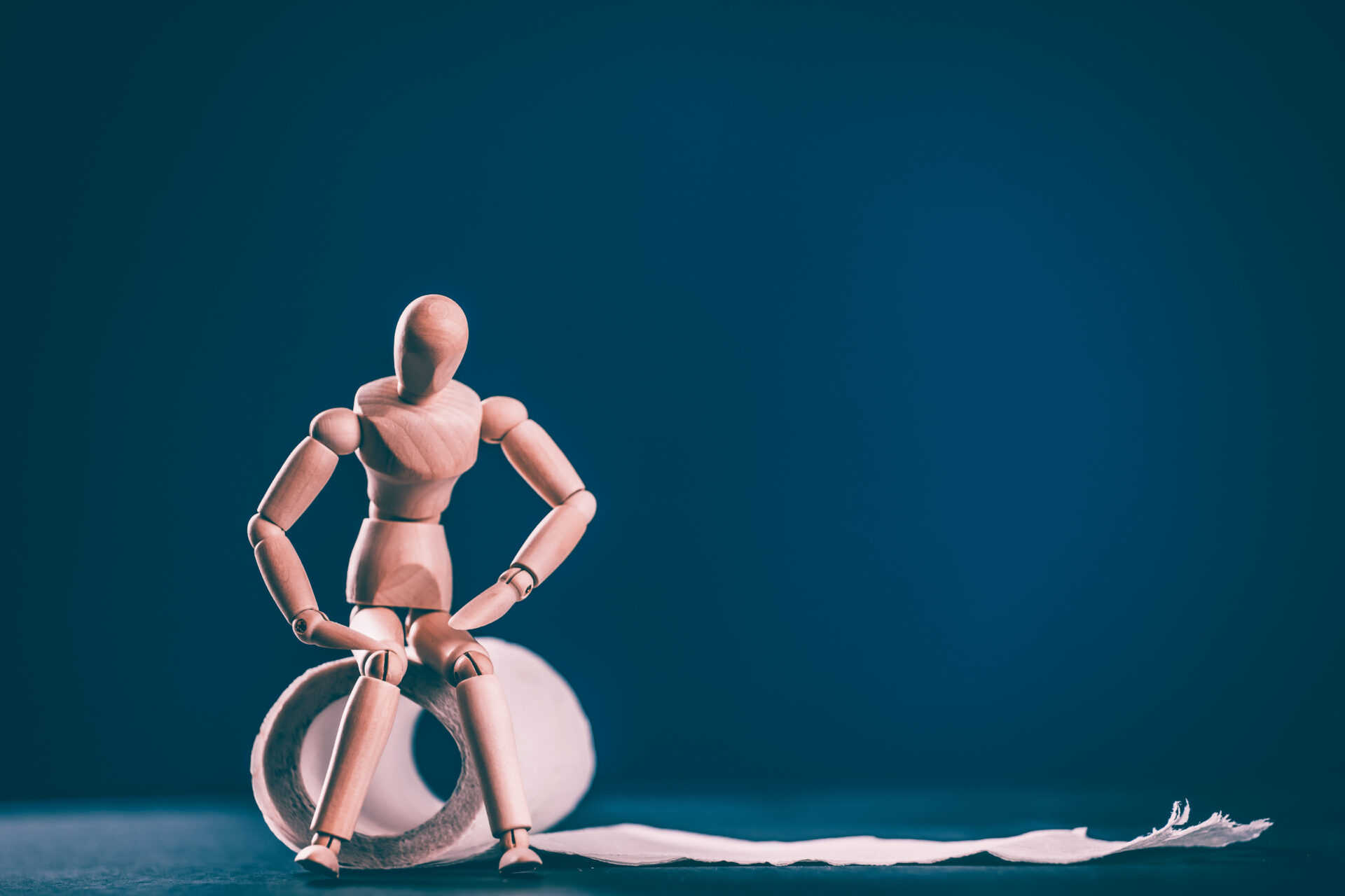 Wooden man with roll of toilet paper on blue background. Bowel problems, incontinence and diarrhea concept.