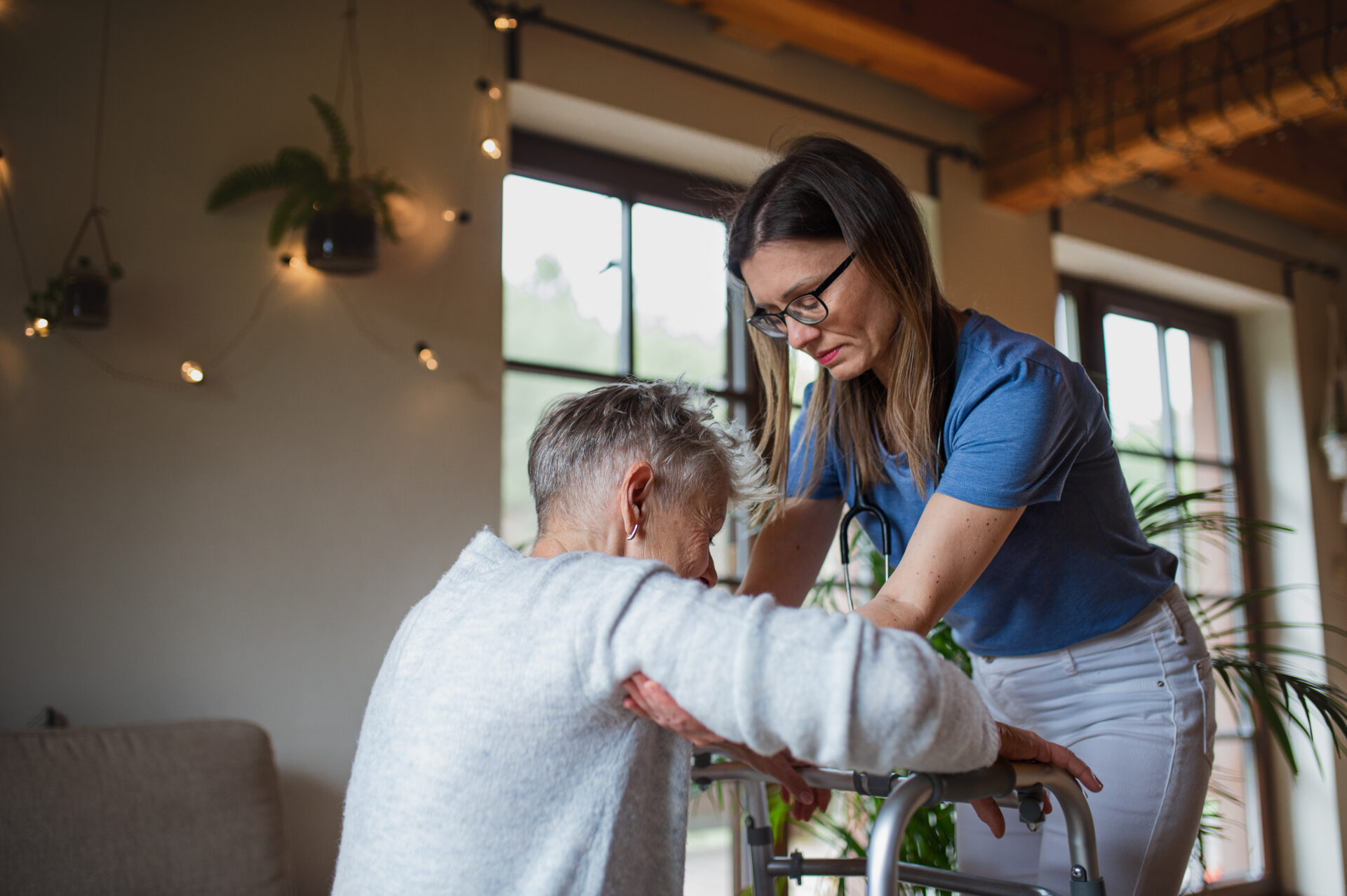 A care professional visiting senior woman indoors at home, helping her to walk.