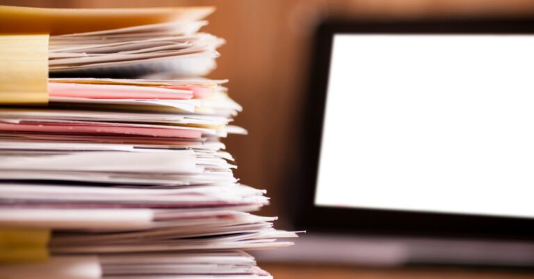 Stack of paperwork next to a computer screen